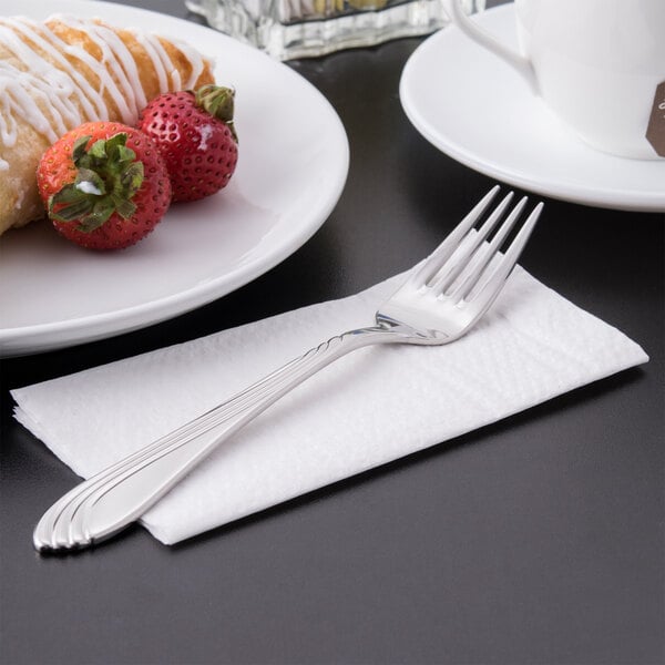 A Libbey stainless steel dessert fork on a napkin next to strawberries.