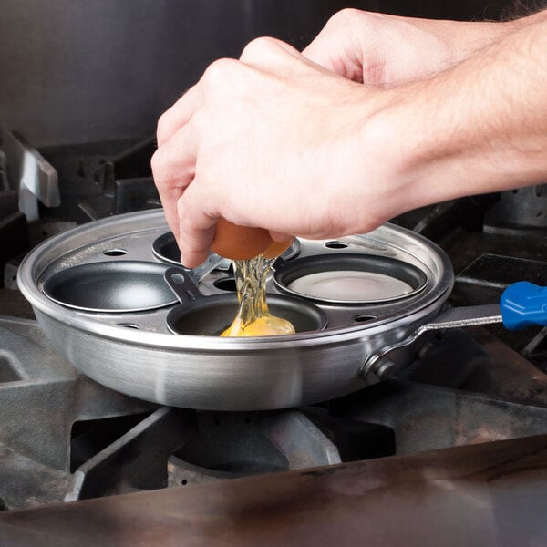 A person using the Vollrath Wear-Ever aluminum egg poacher pan to cook eggs on a stove.