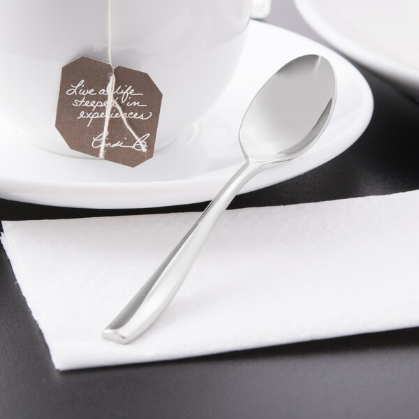 A Libbey stainless steel demitasse spoon on a white plate with a brown paper tag tied to a white tea cup.