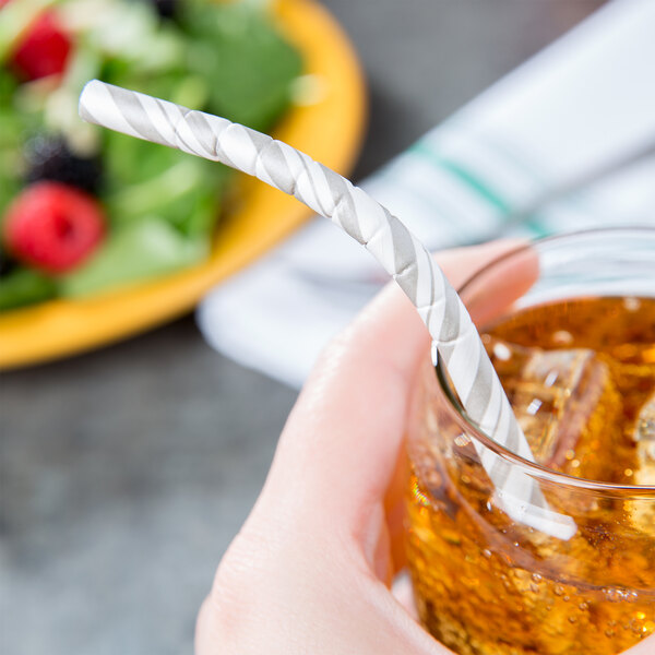 A hand holding a glass of liquid with a Creative Converting white and silver striped paper straw.
