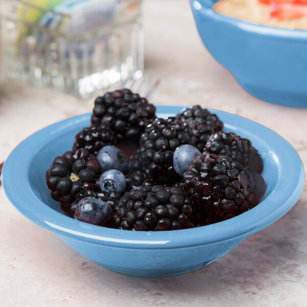 A close up of a Libbey blueberry porcelain fruit bowl filled with blackberries and blueberries on a table.
