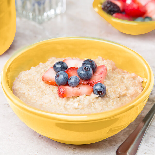A close up of oatmeal with strawberries and blueberries in a yellow Libbey Cantina bowl.