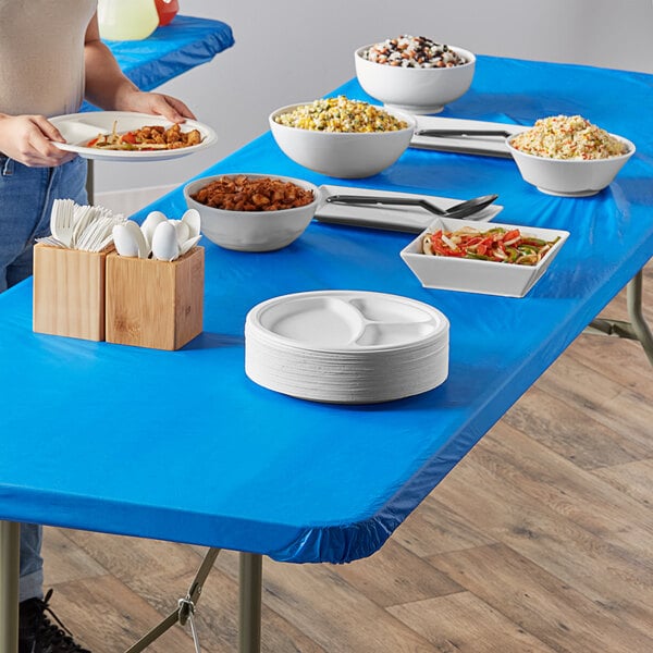 A blue rectangular table with white bowls and plates of food on it.