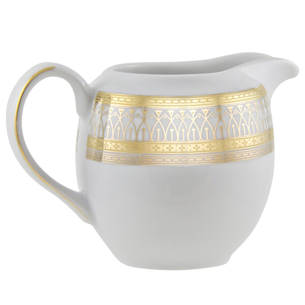 A white porcelain creamer with gold accents and a gold handle.