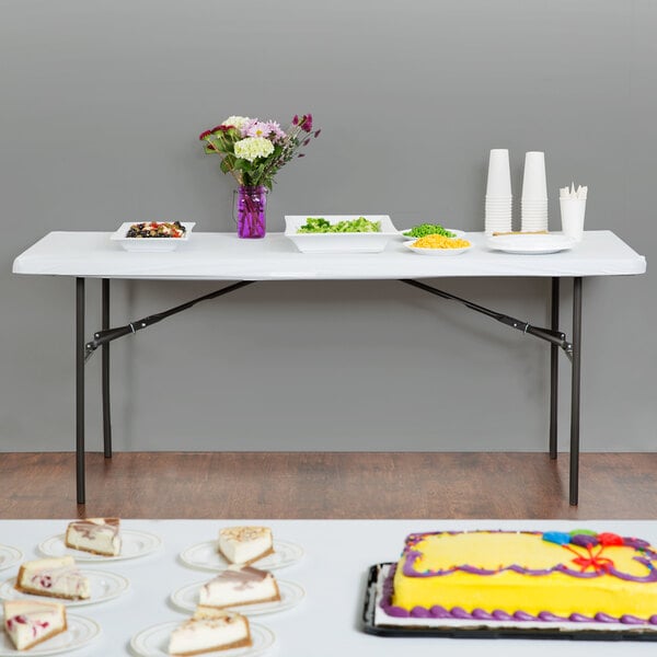 A white rectangular plastic tablecloth with elastic on a table with food on it.