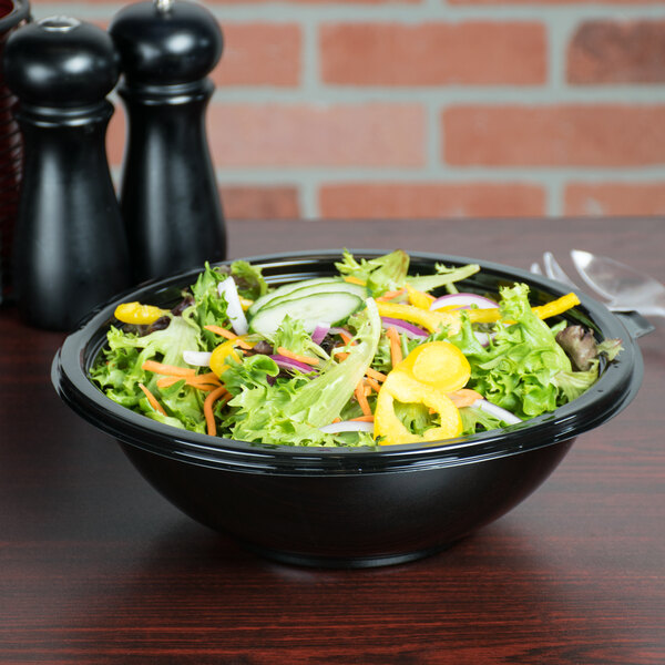 A bowl of salad with vegetables in a black Fineline Super Bowl on a table.