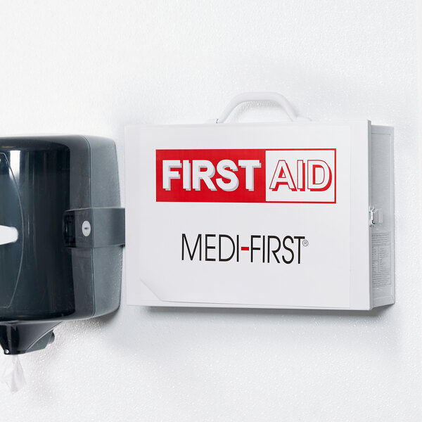 A Medique first aid kit cabinet on a wall with a white sign with red text.