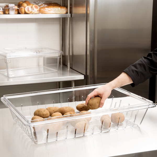 A woman using a Cambro clear plastic food drain box to hold potatoes.