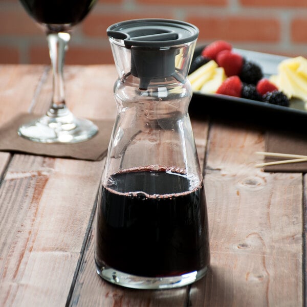 An Arcoroc glass carafe filled with red liquid on a table in a winery cellar.
