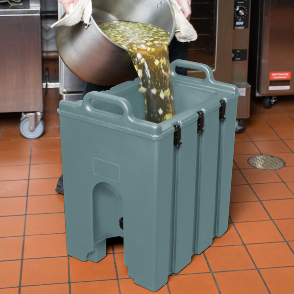 A person pouring soup into a Cambro insulated soup carrier.