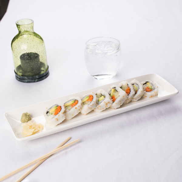 A CAC white porcelain platter with a sushi roll and chopsticks on a table.