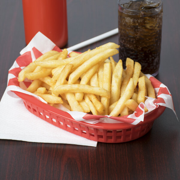 A Tablecraft red plastic oval fast food basket filled with fries and a drink on a table.