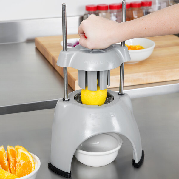 A person using a Vollrath Wedgemaster II to wedge an orange over a bowl.