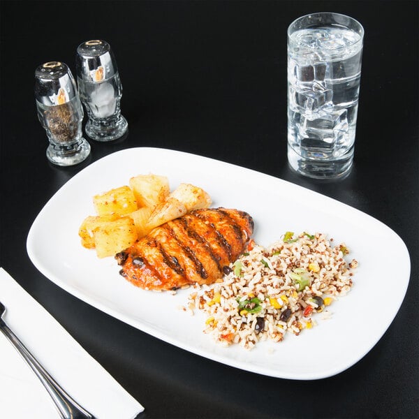 A Libbey ultra bright white porcelain coupe platter with chicken and rice on it next to a glass of water.