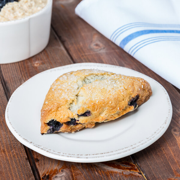 A blueberry scone on a Libbey Farmhouse porcelain plate on a table in a bakery display.