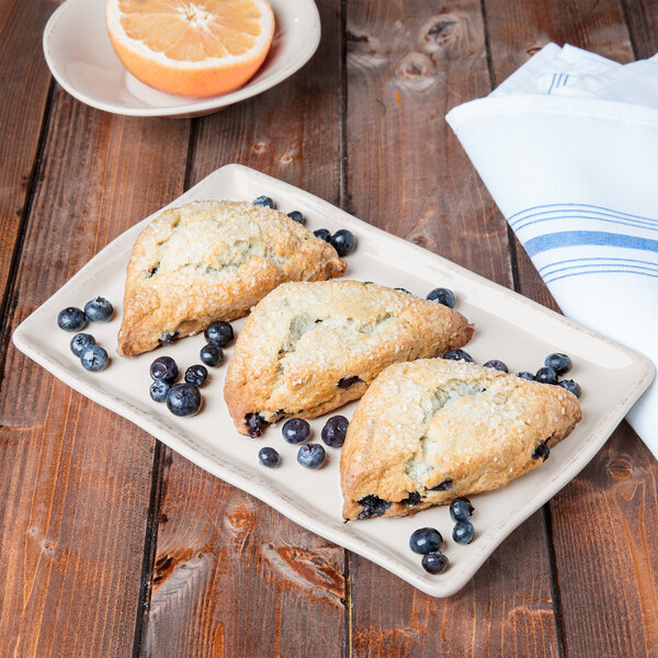 A rectangular ivory porcelain tray with blueberry scones and orange slices on it.