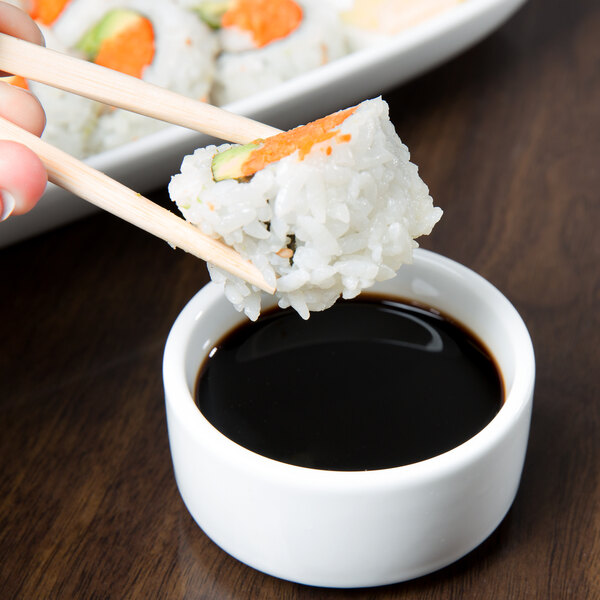 A hand holding chopsticks over a bowl of sushi with Libbey Ultra Bright White Monorail Bowl filled with soy sauce.