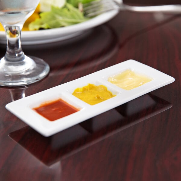A Libbey porcelain tray with three wells holding condiments on a table.