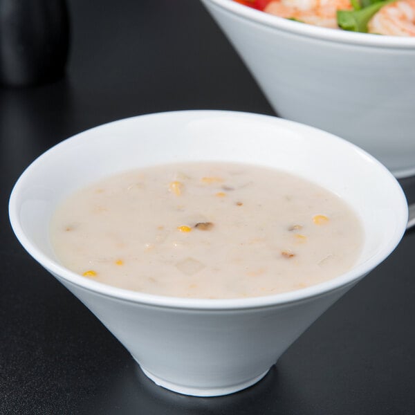 A Libbey white porcelain bowl of soup next to a bowl of salad.