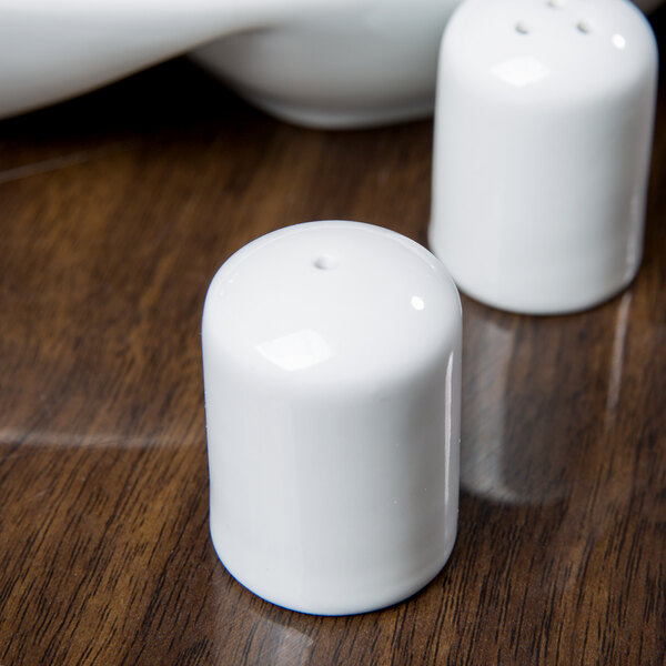 A Libbey white porcelain salt shaker on a wood table.