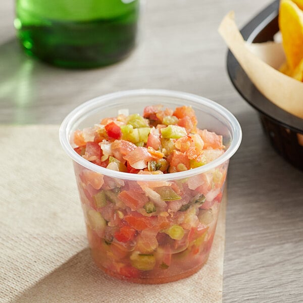 A clear plastic Choice souffle cup of salsa with a bowl of chips.