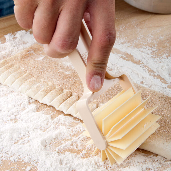A person using an Ateco plastic bear claw dough cutter to cut dough.