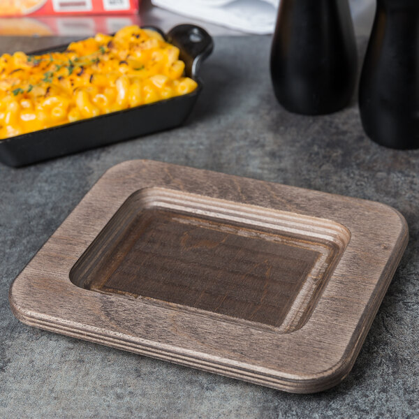 A Lodge rectangular wooden underliner with a walnut finish under a wooden plate of macaroni and cheese.