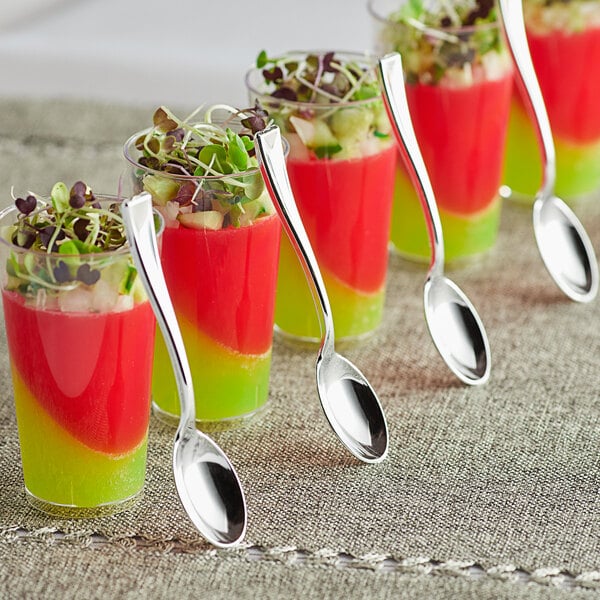 A close-up of a Visions silver plastic tasting spoon in a glass with watermelon and vegetables.