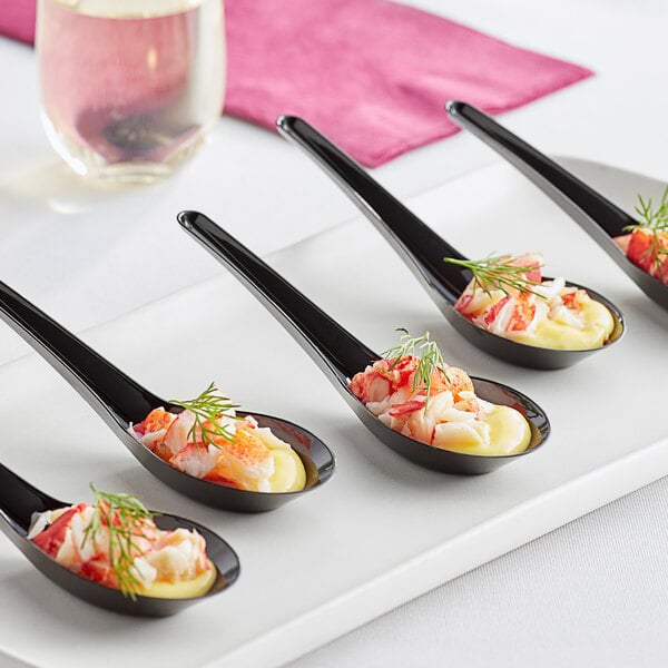 A white plate with four black Visions plastic Asian soup spoons filled with food.