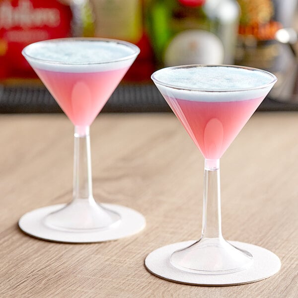 Two Visions clear plastic martini cups filled with pink liquid on a table.