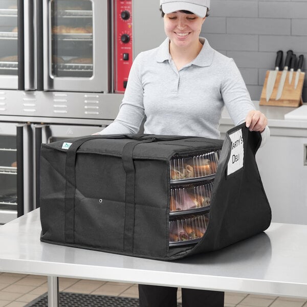 A woman holding a black Choice insulated deli tray bag with food inside.