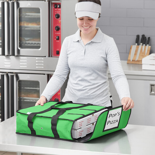 A woman holding a green Choice insulated pizza delivery bag with pizzas inside.