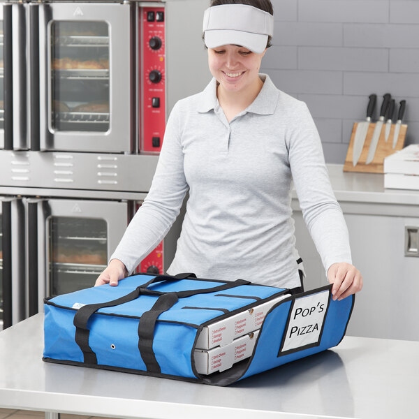 A woman wearing a cap holding a blue Choice insulated pizza delivery bag with white pizza boxes inside.