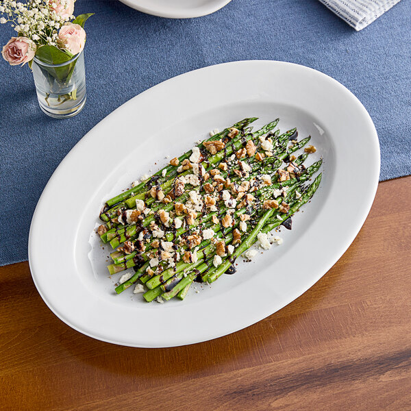 An Acopa Bright White wide rim stoneware platter with rolled edges holding asparagus, feta cheese, and nuts.