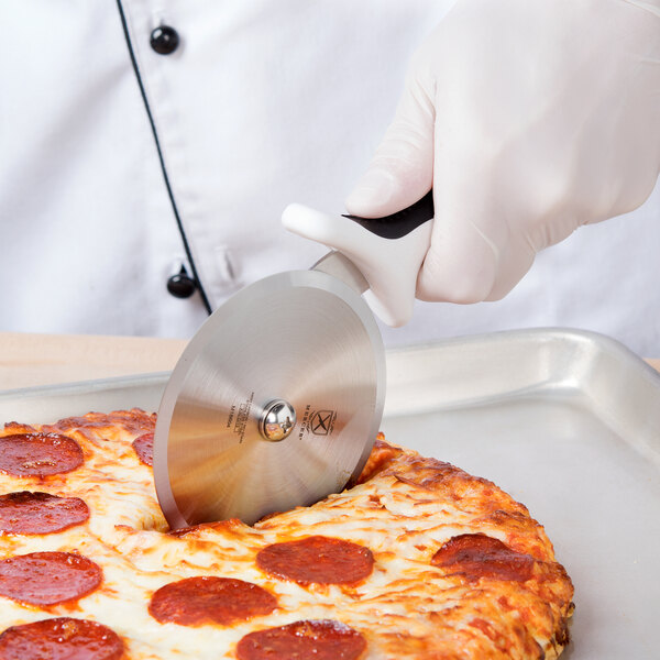 A person using a Mercer Culinary 4" pizza cutter to cut a pizza.