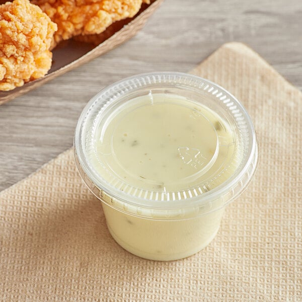 A plastic container of white sauce with a Choice PET plastic lid next to fried chicken.