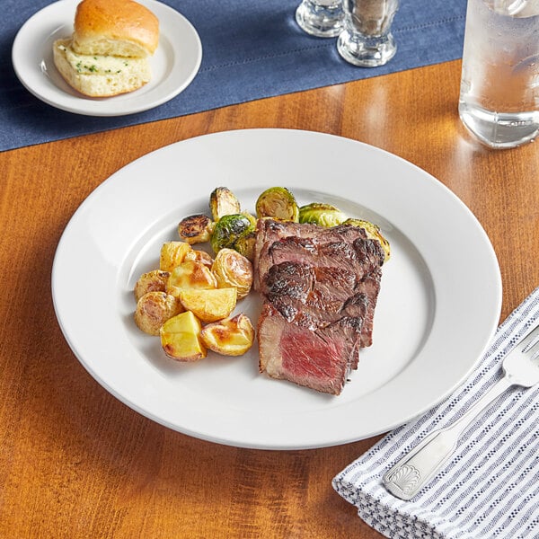 An Acopa Bright White wide rim stoneware plate with a steak and potatoes on it.