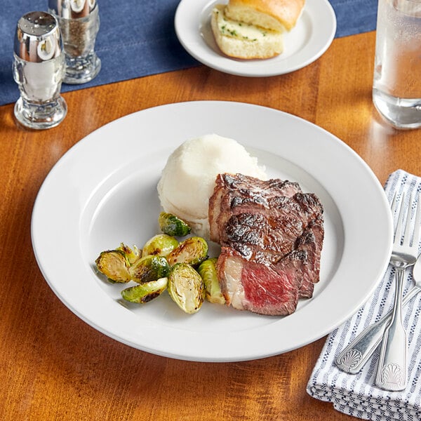 An Acopa bright white stoneware plate with a piece of meat and mashed potatoes on a table.