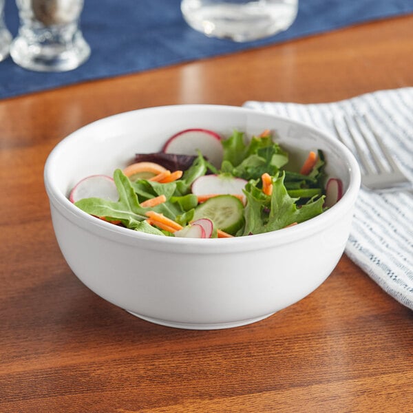 A table set with a bright white Acopa stoneware bowl filled with salad.