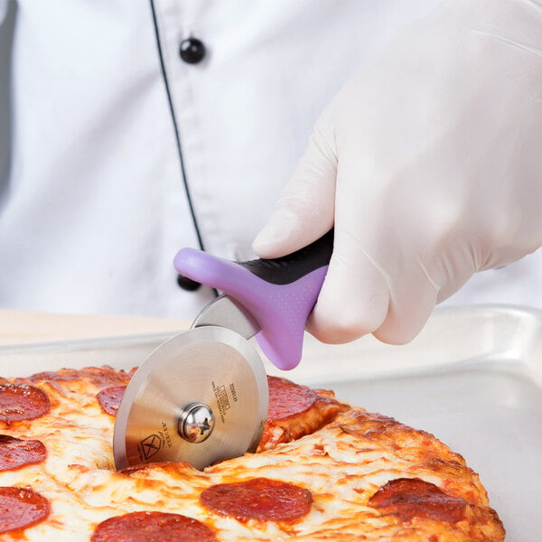 A gloved hand with a purple Mercer Culinary Millennia pizza cutter cutting a pizza.