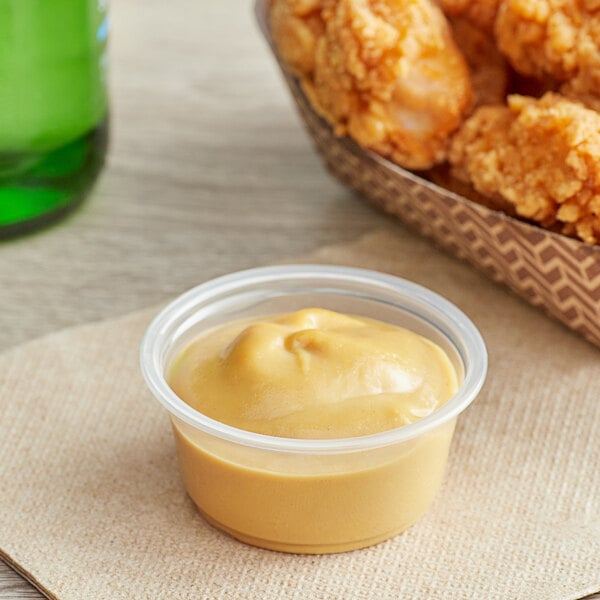 A plastic Choice souffle cup filled with sauce on a table next to a bowl of fried chicken.