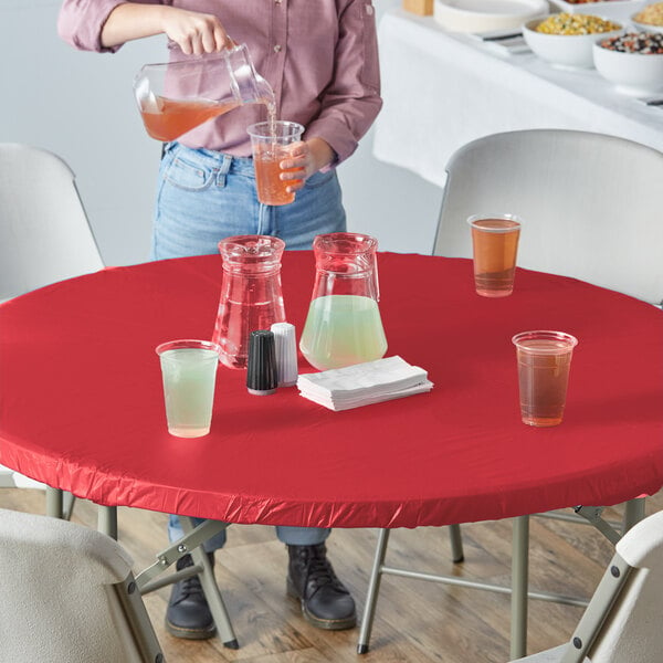 A person pouring a brown drink into a plastic cup on a red table with a Creative Converting red plastic tablecloth.
