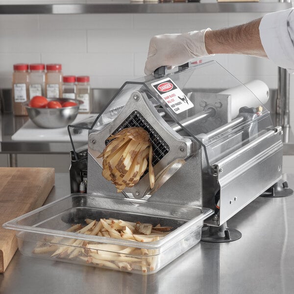 A person using a Nemco Monster Airmatic FryKutter to slice french fries on a counter in a professional kitchen.