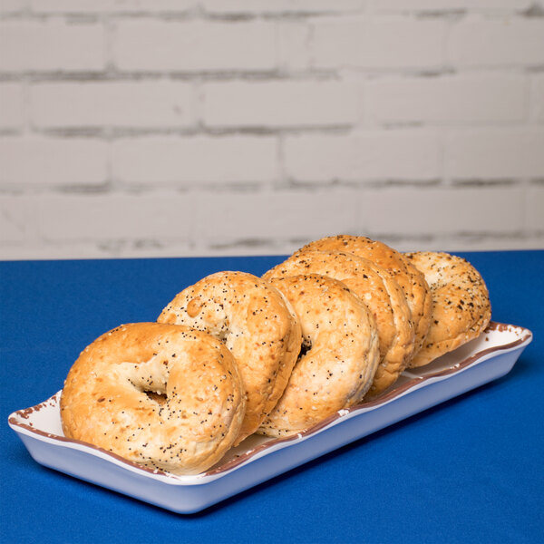 A white rectangular melamine display tray with scalloped edges holding bagels on a blue surface.