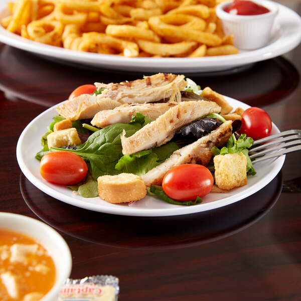 A Carlisle white melamine plate with salad and french fries on it.