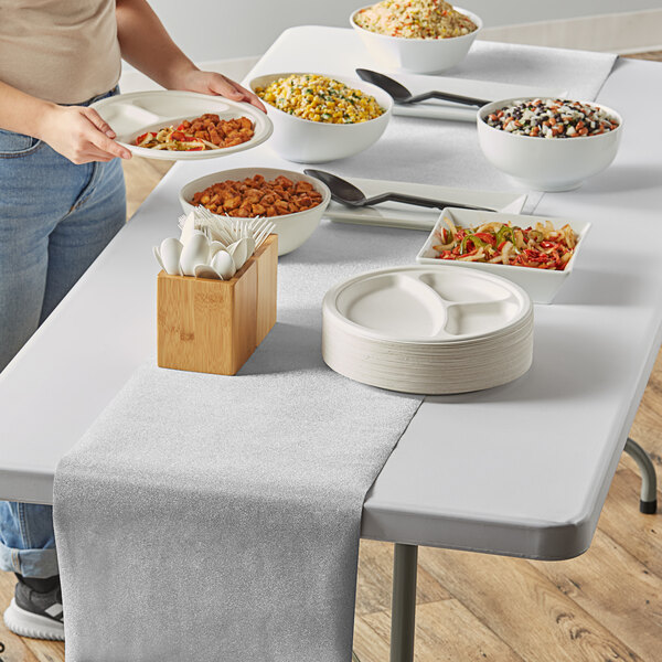 A person serving food on a table with a silver glitter plastic table runner.