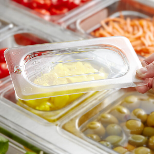 A hand using a Cambro 1/9 size clear plastic lid on a container of food.