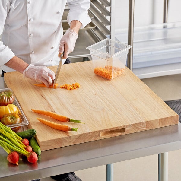 A chef cutting vegetables on a Choice wooden cutting board.