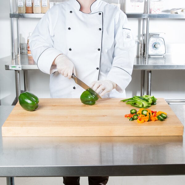 A woman in a chef's uniform cutting a green bell pepper on a Choice wood cutting board.