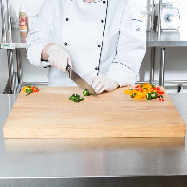 A woman in a chef's uniform cutting peppers on a Choice wood cutting board.